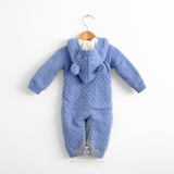 Cornflower blue knit baby one-piece  sweatsuit with a hood, textured cable-knit pattern, and faux-fur fleece lining, hanging on a wooden hanger against a white wall.