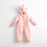 Pastel pink knitted baby jumpsuit with a hood featuring two bear ears and three wooden buttons, fleece lining laid flat on a white background. A watermark at the bottom reads The Vintage Teddy Children's Boutique.