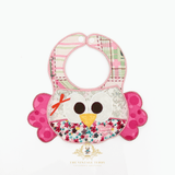 A boutique baby bib with a pretty embroidered patchwork owl-themed, made with floral, plaid and polkadot fabric, and adorned with a pink satin bow, on a white background. The Vintage Teddy's logo is at the bottom center.