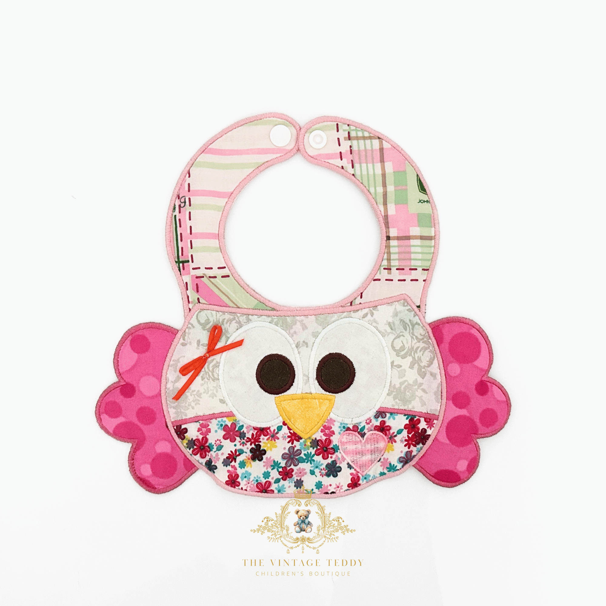 A boutique baby bib with a pretty embroidered patchwork owl-themed, made with floral, plaid and polkadot fabric, and adorned with a pink satin bow, on a white background. The Vintage Teddy's logo is at the bottom center.
