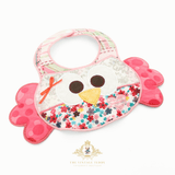 A handmade owl-themed patchwork baby bib, featuring a pink polka-dot wing, and embroidered details, displayed at an angle on a white background. The Vintage Teddy watermark at the bottom