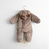 Baby & Toddlers hooded one-piece romper in a soft taupe-brown plush fleece fabric, hanging on a wooden hanger, against a plain white wall. The hood features two small brown faux-fur ear accents, and the romper has long sleeves and footless leg