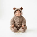 Baby boy sitting wearing a cozy, plush brown hooded one-piece outfit with bear ears on the hood, and footies against a seamless white studio background.