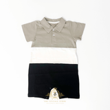 A children's short-sleeve polo shirt one-piece bodysuit laid flat on a white background, featuring color-blocked sections of taupe, white, and black, with a small buttons and pointed collar.