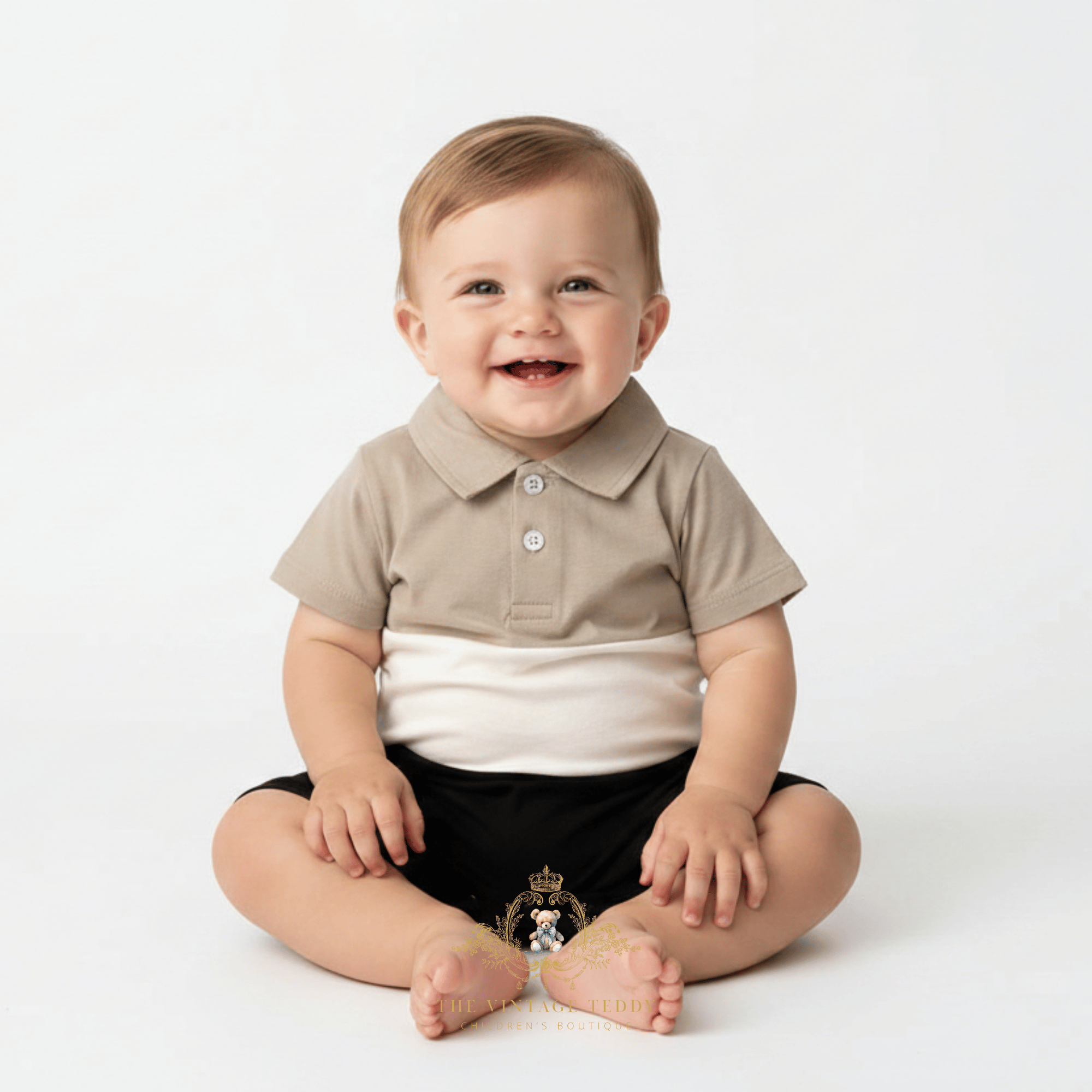 A smiling baby sitting on a white studio background, wearing a short-sleeve polo one-piece romper with a beige collar and upper chest, a white horizontal band, and black shorts.