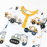 A close-up of a baby short-sleeve one-piece romper  with a white base and a colorful cartoon construction vehicle print, featuring a yellow collar and three-quarter buttons.