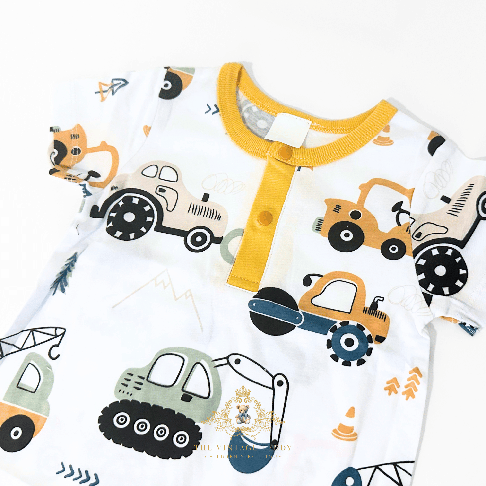 A close-up of a baby short-sleeve one-piece romper  with a white base and a colorful cartoon construction vehicle print, featuring a yellow collar and three-quarter buttons.