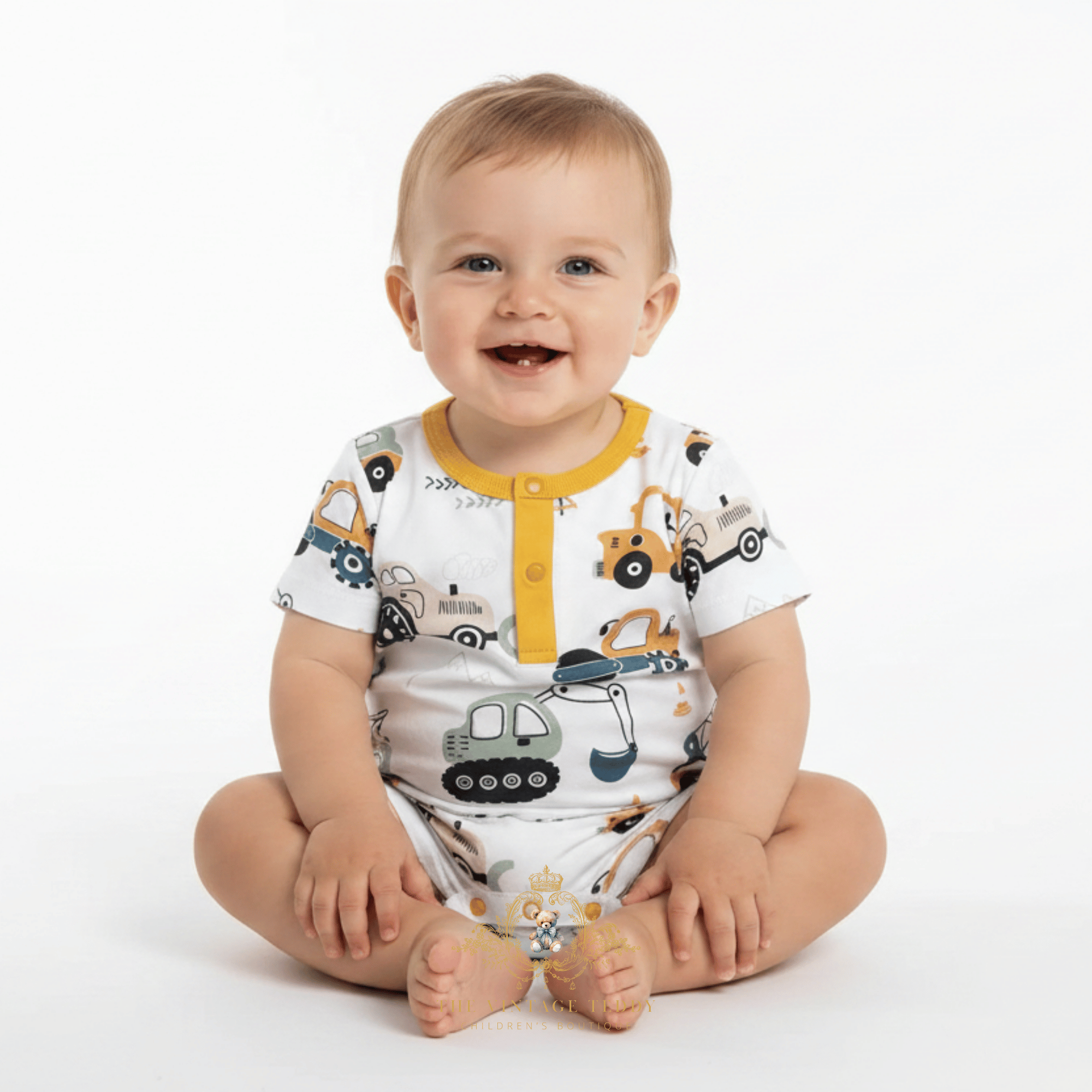 A baby on a white studio background, wearing a white short-sleeve romper printed with construction vehicles and featuring a yellow collar and three yellow buttons.