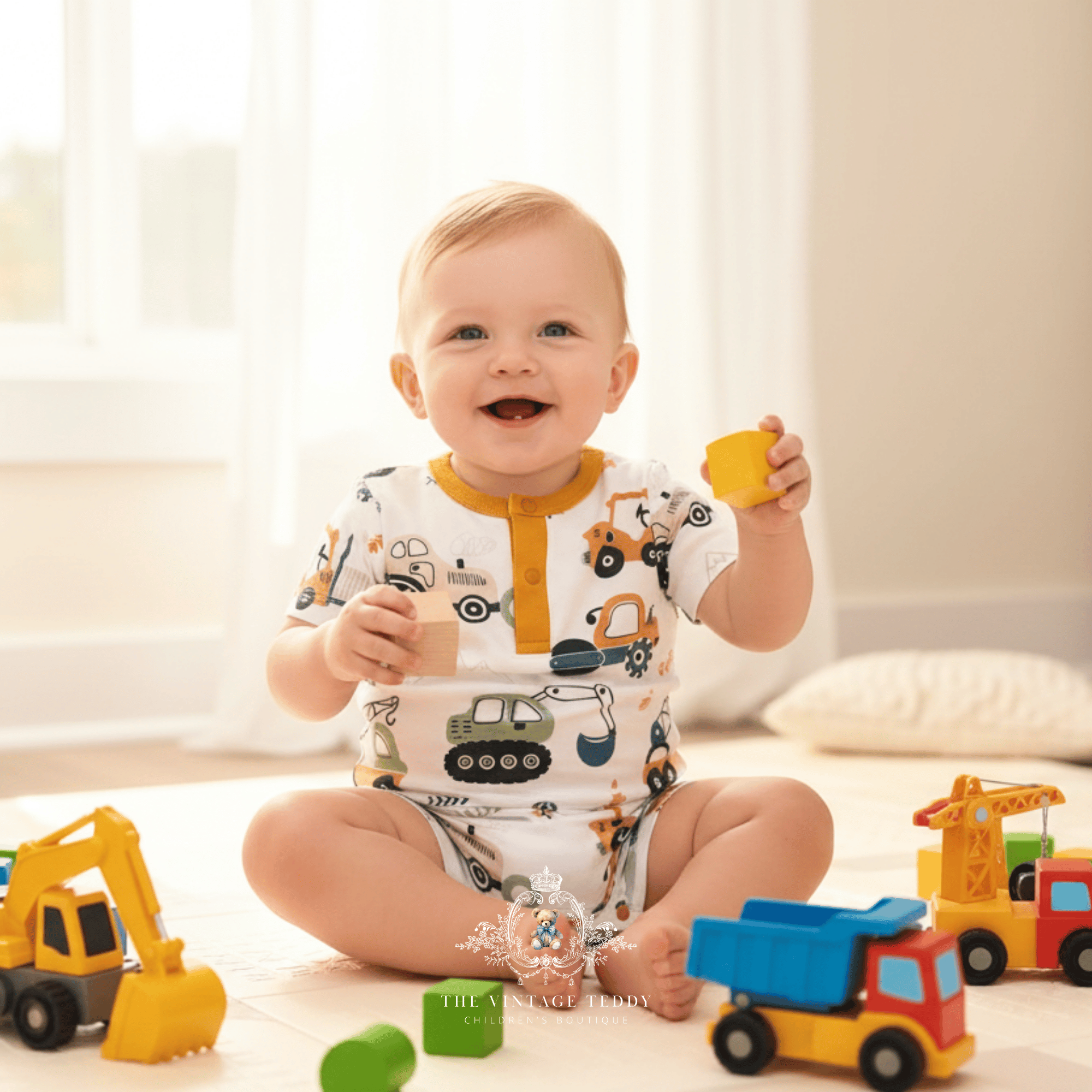 A baby sitting on a light floor playing with colorful toy vehicles, wearing a white short-sleeve romper printed with construction vehicles like excavators, cranes, and dump trucks.
