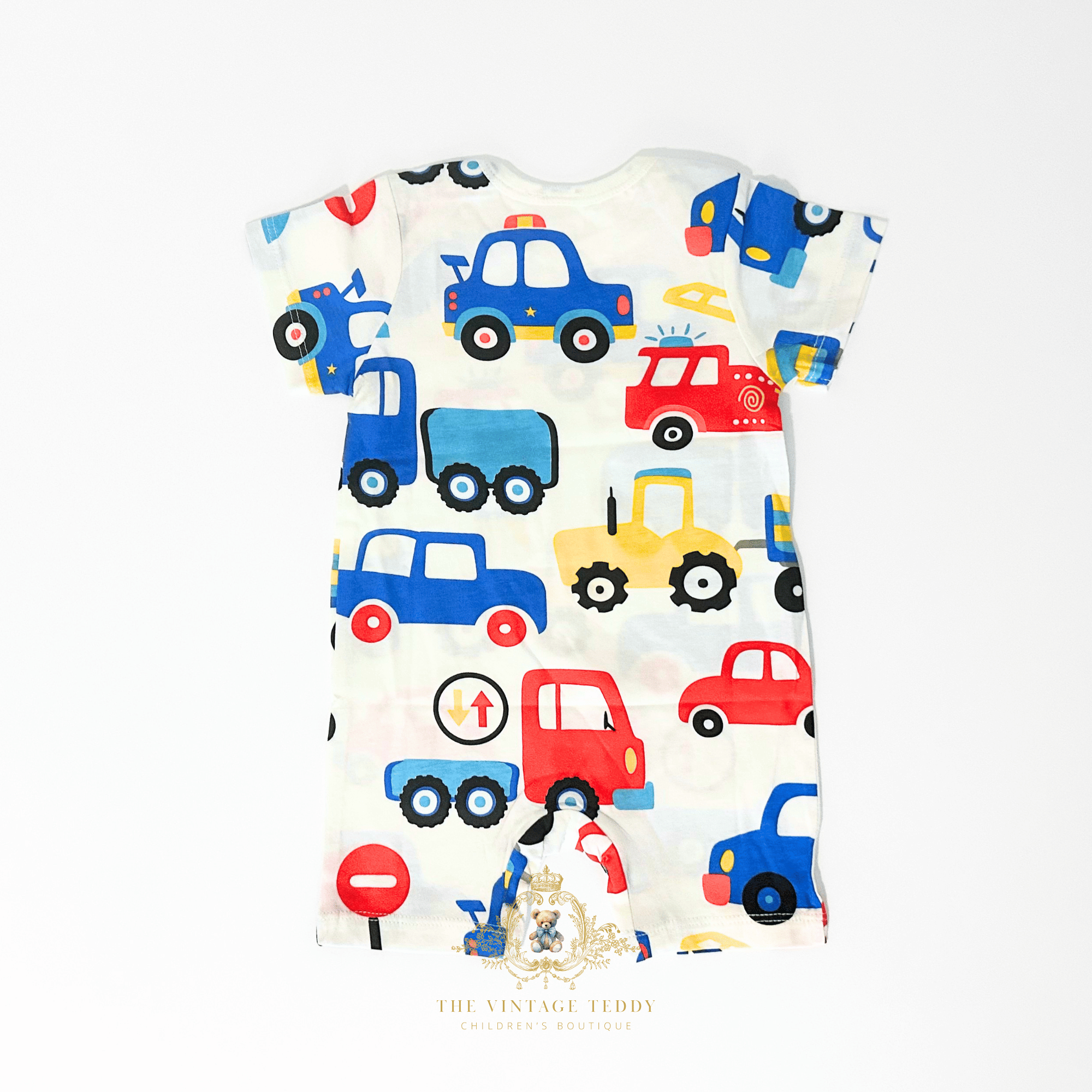 The back of a short-sleeve baby one-piece romper shorts with an all-over colorful cartoon vehicle print, laid flat on a white background. The pattern features blue, red, yellow, and black vehicles on a white base.