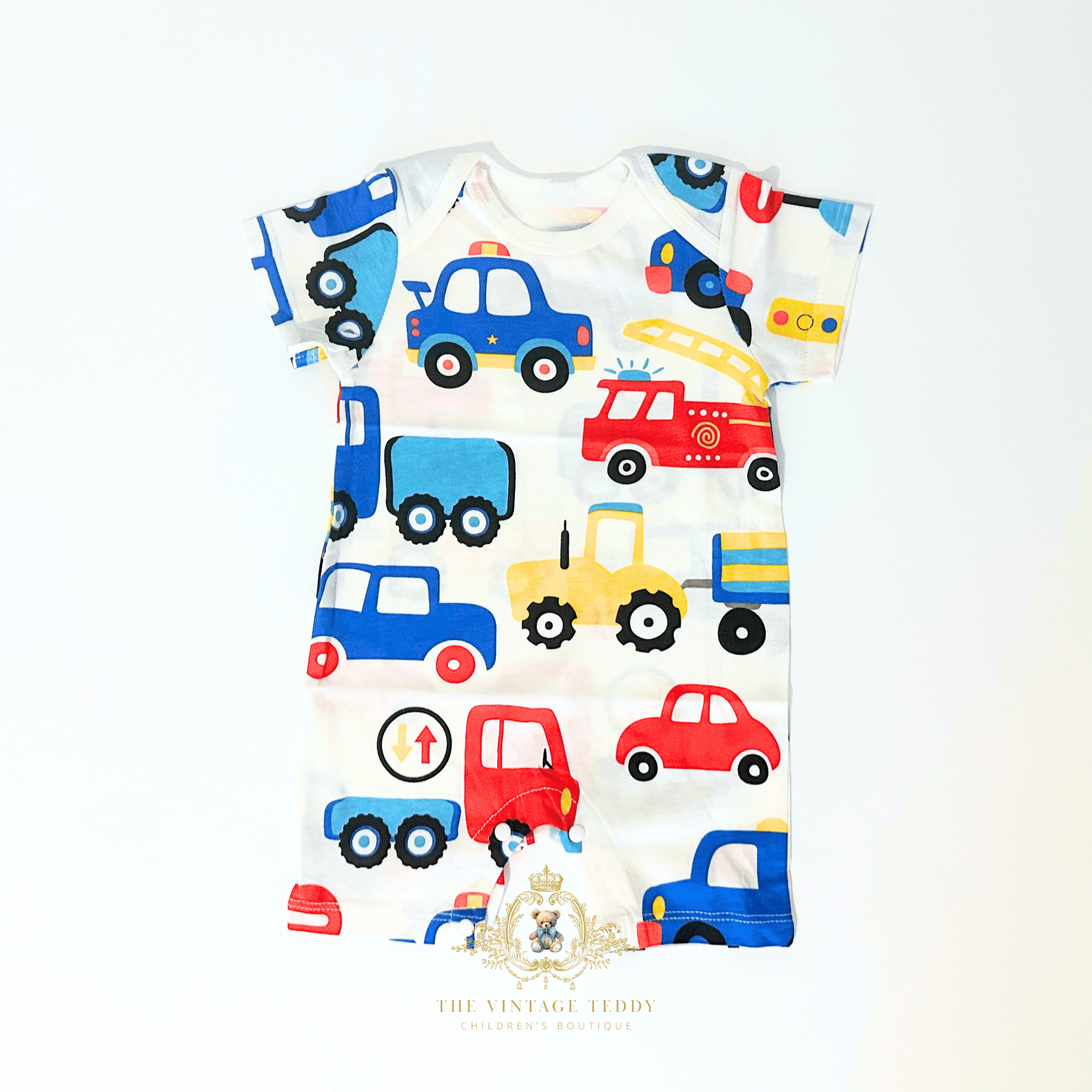 A baby short-sleeve romper with an all-over colorful cartoon truck print on a white background. The print features blue, red, yellow, and black vehicles.