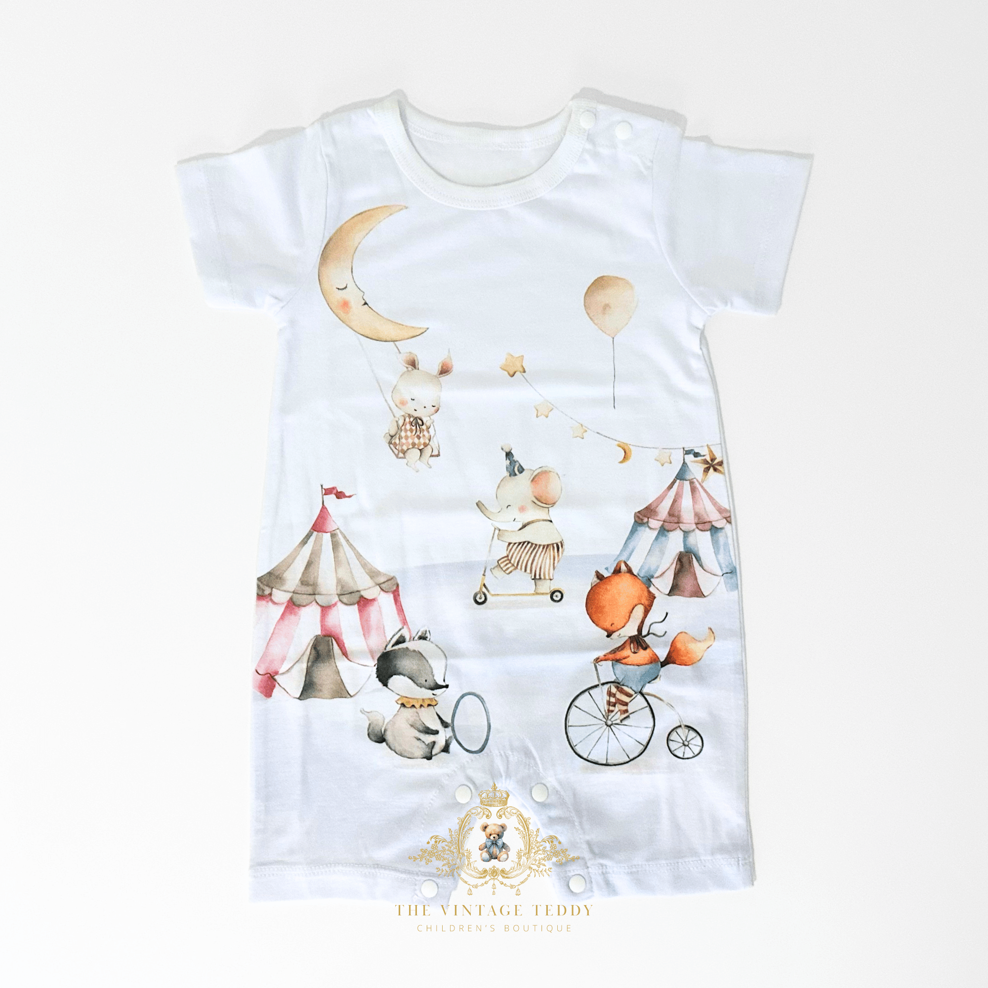 A white short-sleeve baby romper with a whimsical circus-themed watercolor print, featuring a crescent moon, balloons, tents, and animals. The brand logo 'The Vintage Teddy' is visible at the bottom.