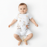 A baby lying on their back wearing a white short-sleeve bodysuit with a whimsical cartoon print of a moon, hot air balloon, bicycle, and tent. The photo is taken on a clean white background with The Vintage Teddy's watermark at the bottom.