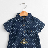 Closeup of navy blue baby romper one-piece outfit with white arrow pattern hanging on a hanger against a white background Cute baby & toddler apparel form The Vintage Teddy Children's Boutique shop.