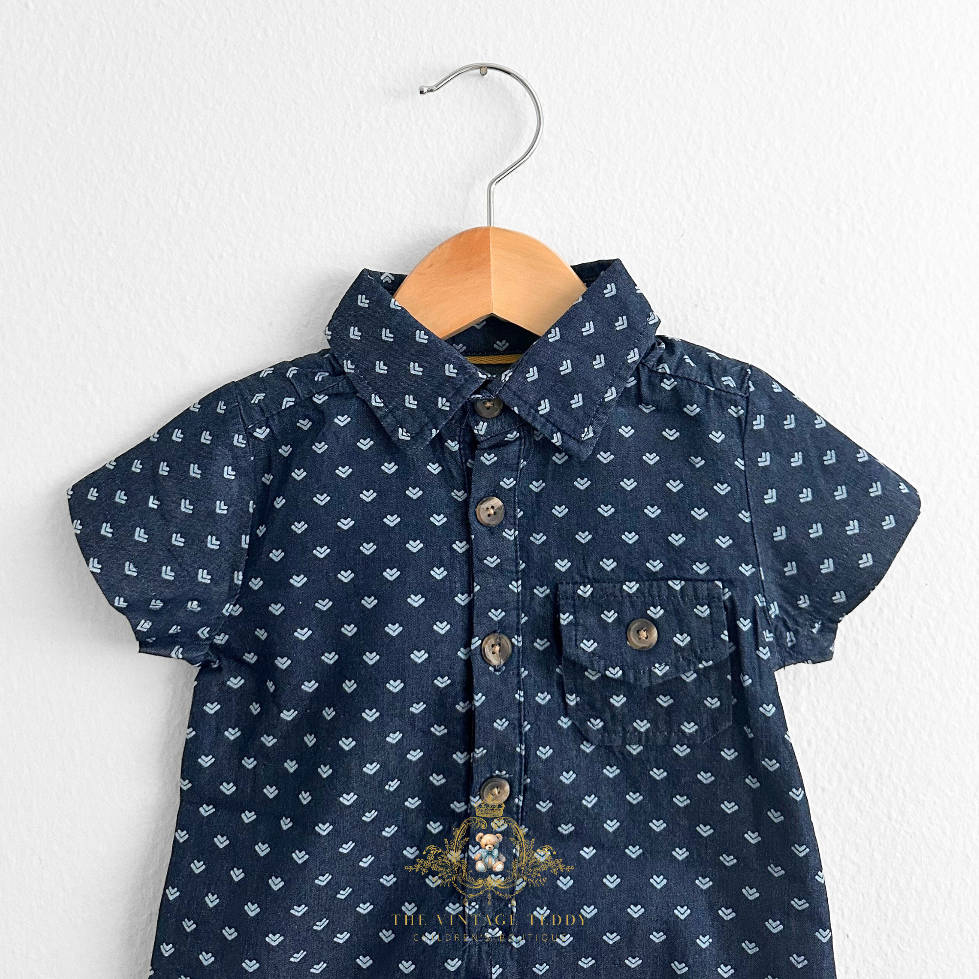 Closeup of navy blue baby romper one-piece outfit with white arrow pattern hanging on a hanger against a white background Cute baby & toddler apparel form The Vintage Teddy Children's Boutique shop.