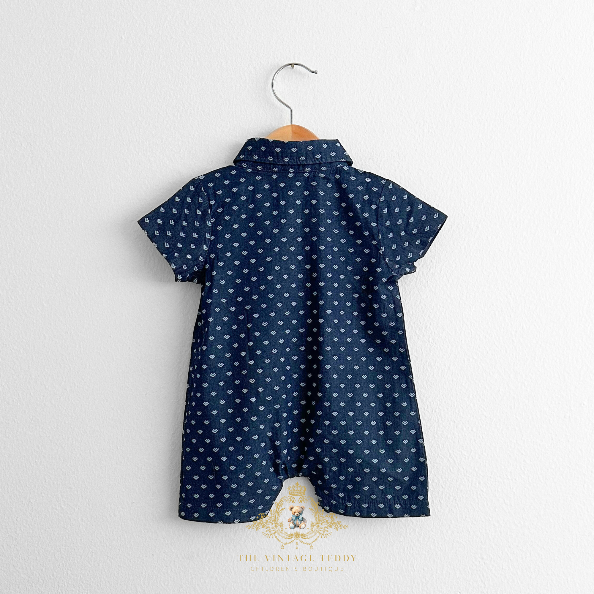 Baby & Toddler one-piece rompers with a navy blue and white arrow print pattern displayed on a hanger against a white wall  background, clothing for kids from The Vintage Teddy Children's Boutique.