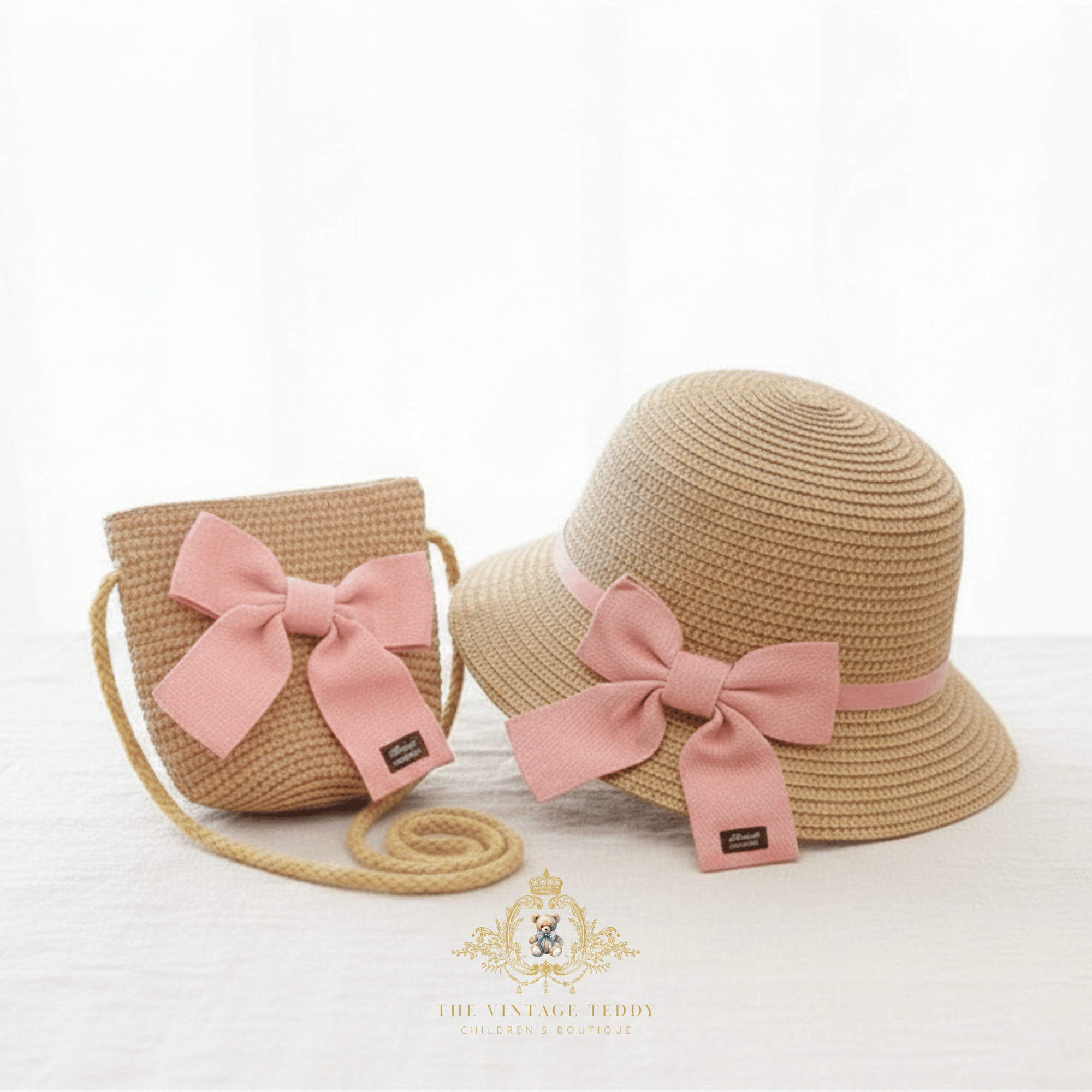 A kids straw sun hat and matching woven crossbody bag in beige, both decorated with large dusty pink bows and pink bands, displayed on a white surface against a white background. A logo for 'The Vintage Teddy' is visible at the bottom.