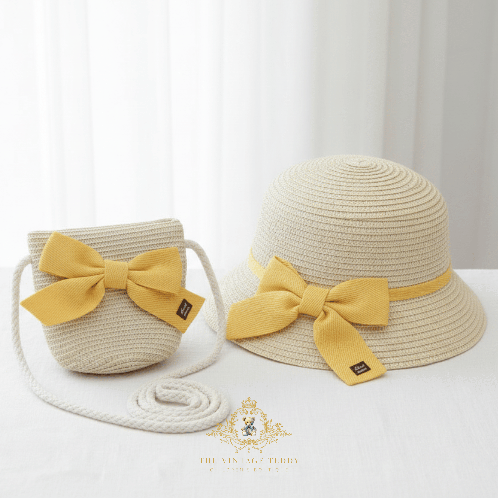 A straw bucket hat and matching woven shoulder bag set for children in a light beige color, both featuring a prominent yellow fabric bow with a small black brand tag. The bag has a thick white rope strap coiled in front.