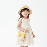 A young girl wearing a straw sun hat and matching handbag, smiling in a cream  children's dress, the kids accessories is adorned with a yellow ribbon, in bright background studio setting. The Vintage Teddy's brand logo is visible at the bottom of the image.