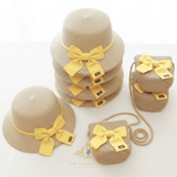Stacks of kids straw sun hats and matching kids handbags,  the accessories are adorned with yellow ribbons, on white surface in light studio background. The Vintage Teddy's brand logo is visible at the bottom of the image.