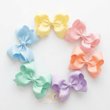 Six large grosgrain girls hair bows in pastel shades of yellow, baby blue, pink, peach, mint green, and lavender, arranged in a circle on a white background. The Vintage Teddy brand logo is bottom-center.