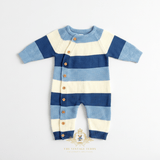 A baby boy knit one-piece romper with horizontal stripes blue and white, featuring a button-down on the side front with wooden buttons and ribbed cuffs and round collar, laid flat on a white background surface. 'The Vintage Teddy watermark logo displayed at the bottom center. 
