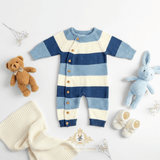 A baby boys knit one-piece romper with horizontal blue and white stripes, styled in a flat lay with a brown teddy bear, blue bunny toy, booties, and a cream knit blanket with baby's breath flowers on a white background. The Vintage Teddy logo firmly stamped at the bottom.