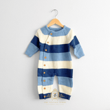 A baby boy knit one-piece romper with horizontal stripes in blues and white, hanging on a natural wooden hanger against a white wall. The baby romper features a button closure down the front side and ribbed cuffs and hem. The Vintage Teddy watermark displayed bottom center.
