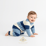 A baby boy crawling on a white studio floor wearing a two-toned blue and white striped knit romper. The brand watermark logo 'The Vintage Teddy' is visible at the bottom center.