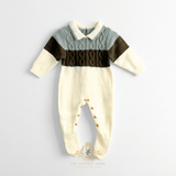 Baby boys knit footed jumpsuit with a color-blocked design. The top portion is a sage green cable-knit collar with a cream  collar, while the middle features a wide olive green band across the chest and sleeve stripe and the bottom is a cream color, laid flat on a white surface background.