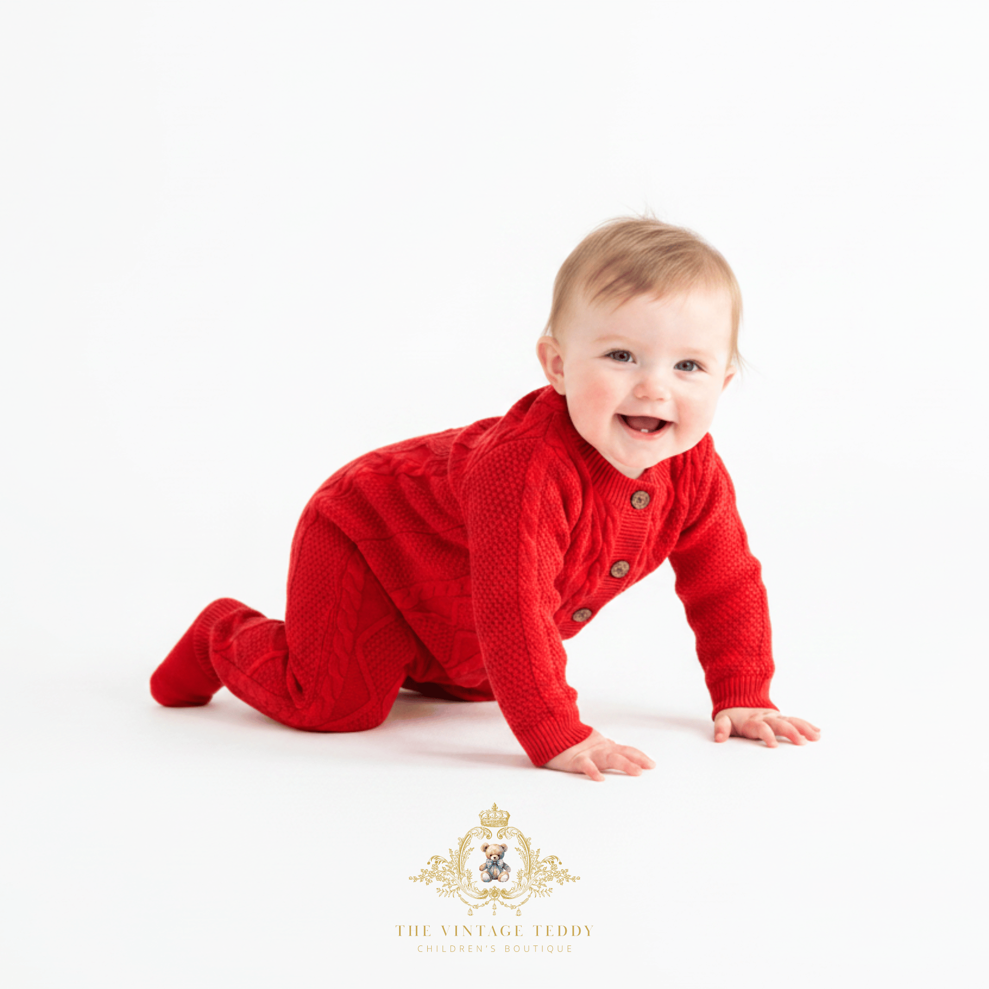 A baby girl crawling on a white studio background wearing a bright red cable-knit sweatsuit with brown buttons. A gold watermark logo for 'The Vintage Teddy' is visible at the bottom.