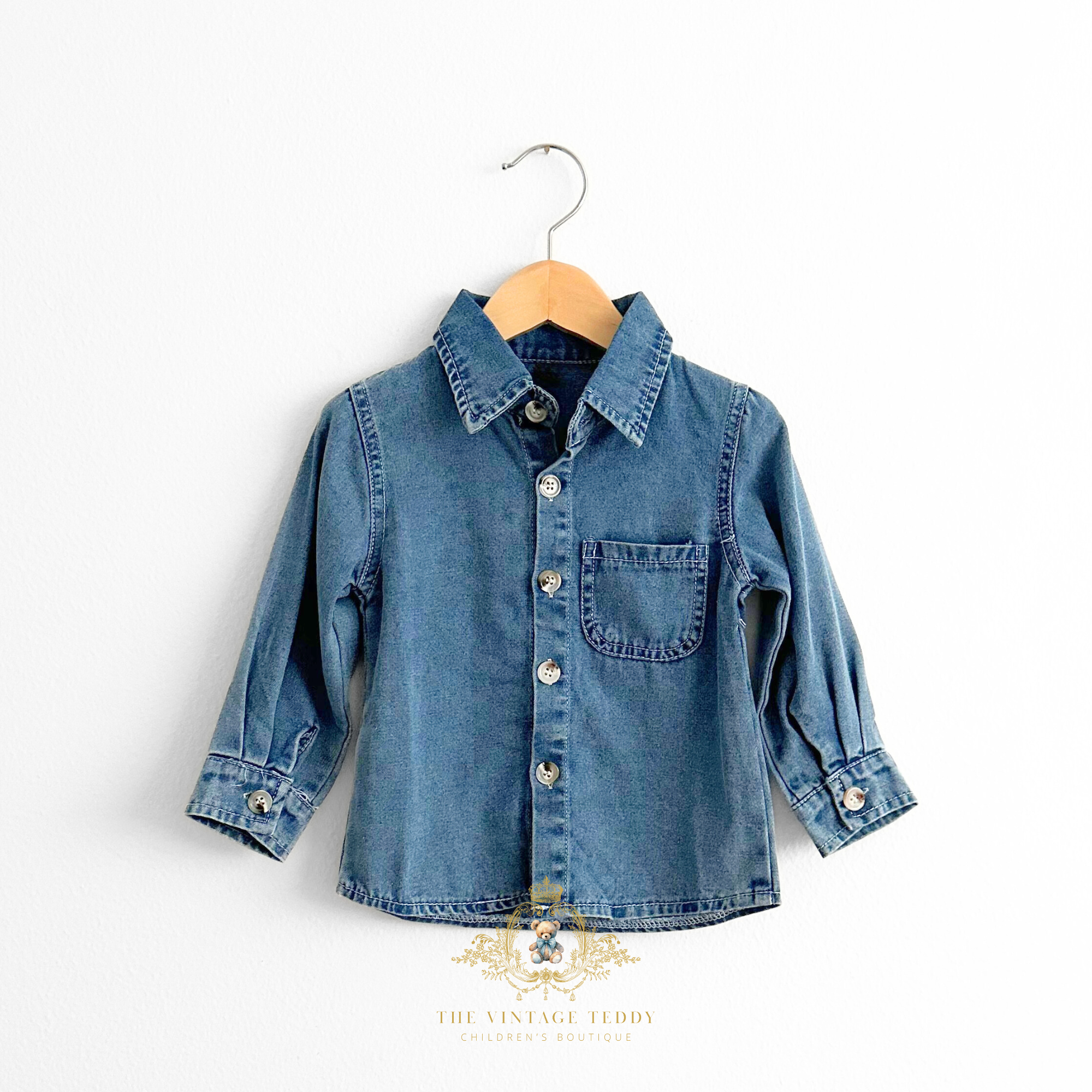 Kids blue denim long sleeve shirt for little boys on a wooden hanger with 'The Vintage Teddy' logo.