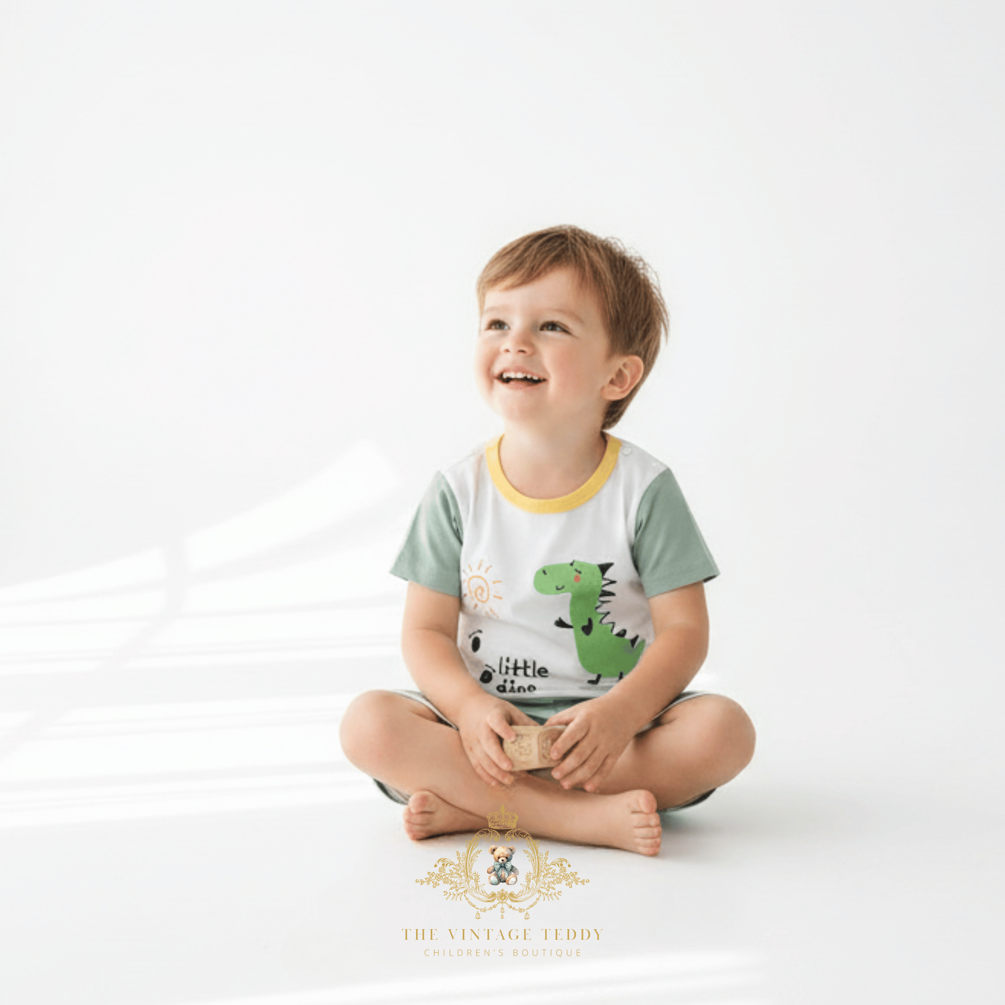 Toddler boy sitting smiling and looking up wearing Little dinosaur matching set boys summer boutique outfit