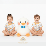 Two children in matching Mr. Duck top & shorts sitting with a large plush duck toy on a white background, models for The Vintage Teddy Children's Boutique