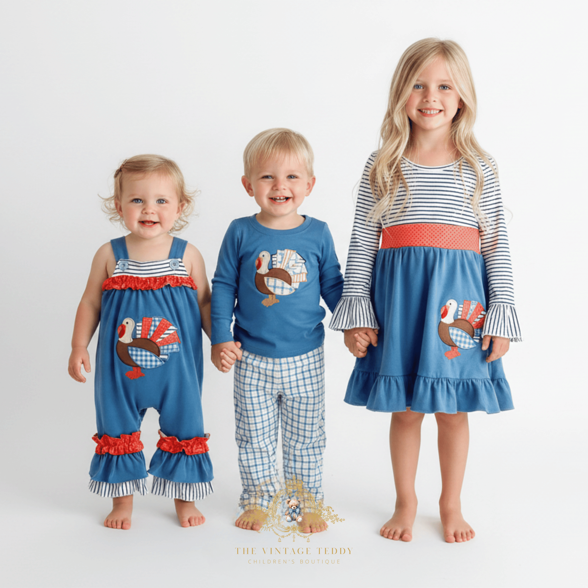 Three children standing together against a clean white studio background, wearing coordinated autumn-themed clothing. The set includes a blue romper with orange  ruffles and an embroidered turkey on the youngest child, a blue long-sleeve shirt with the same embroidery and plaid pants, and a blue long-sleeve dress with a striped bodice, orange waistband, and same embroidered turkey patchwork design.
