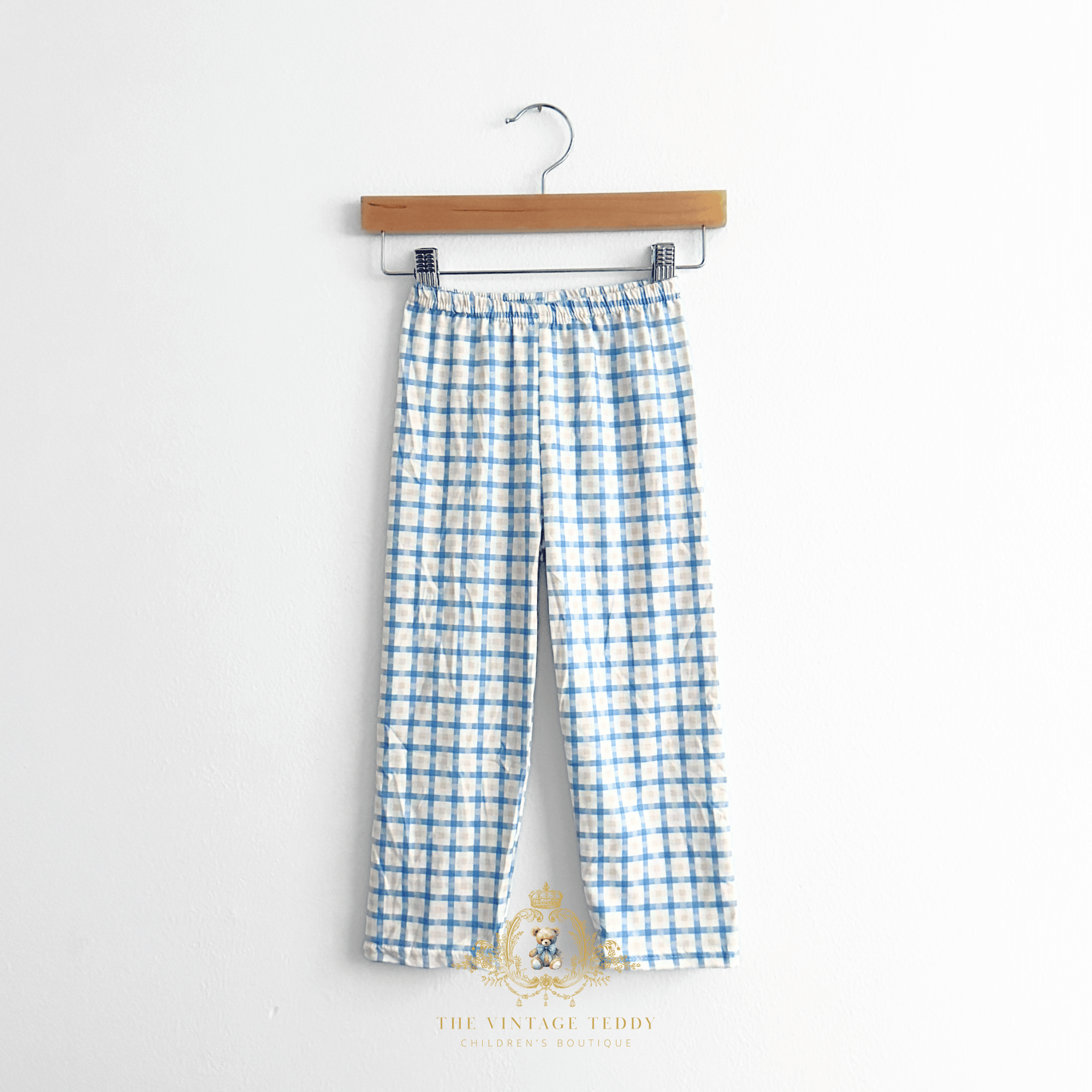 Little boys blue and white checkered long  pants with an elastic waistband hanging from a wooden hanger against a plain white wall.
