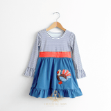 A toddler girl's long-sleeve dress hanging on a natural color wooden hanger against a white wall. The dress has a navy blue and white striped bodice, a coral orange polka dots waistband and a solid blue ruffled hem skirt featuring an embroidered  turkey applique on the front.