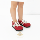 A child wearing red slip-on shoes with white strap details and black soles, shown from the knees down against a clean white background. A 'The Vintage Teddy' brand logo is visible at the bottom.