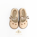 A pair of beige Mary Jane style kids shoes for toddlers, featuring embroidered floral details and a decorative ribbon bow on the strap, shown from a top-down view on a white background.
