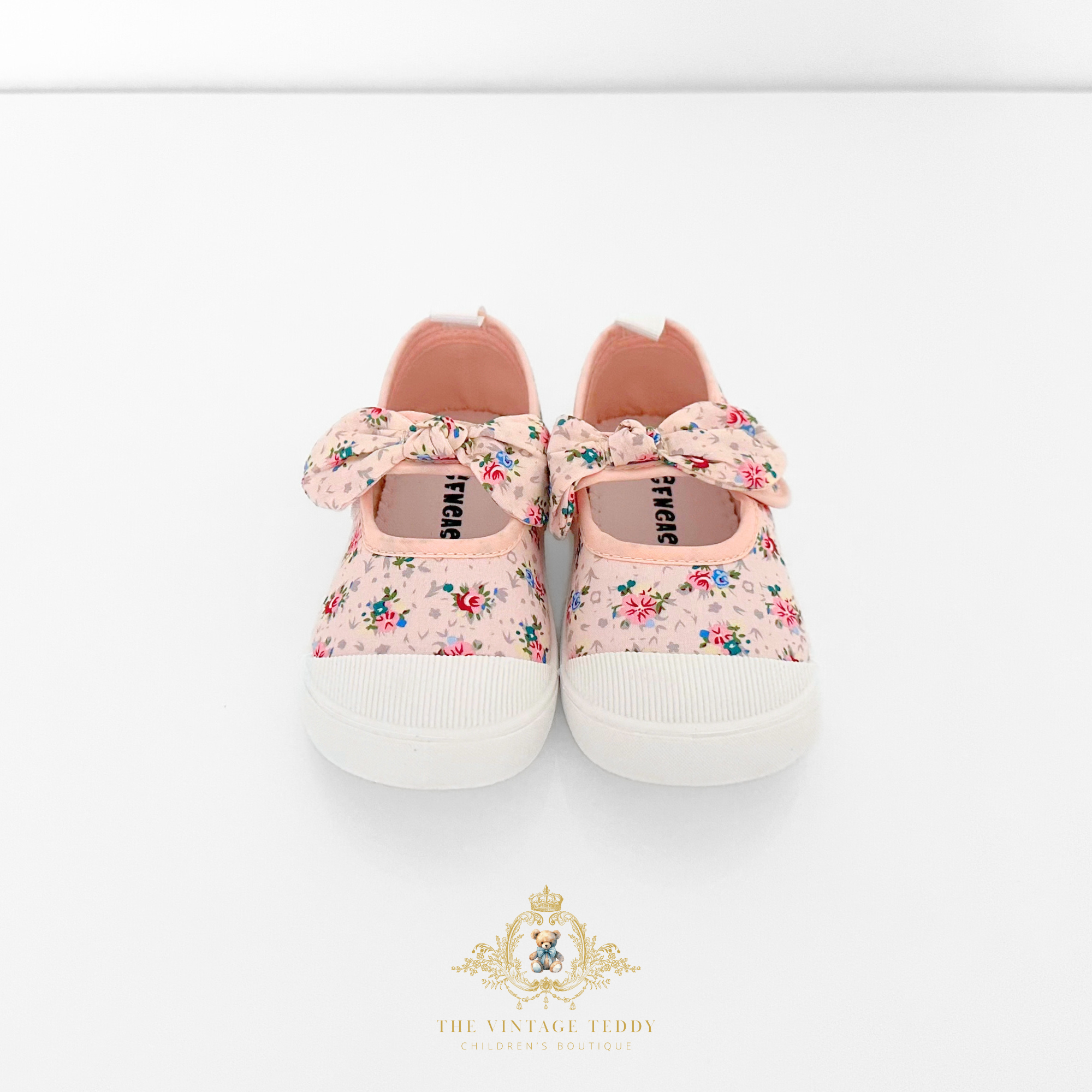 Pretty pair of pink floral baby shoes, kids sneakers with bow and white soles on a light background featured on The Vintage Children's Boutique.
