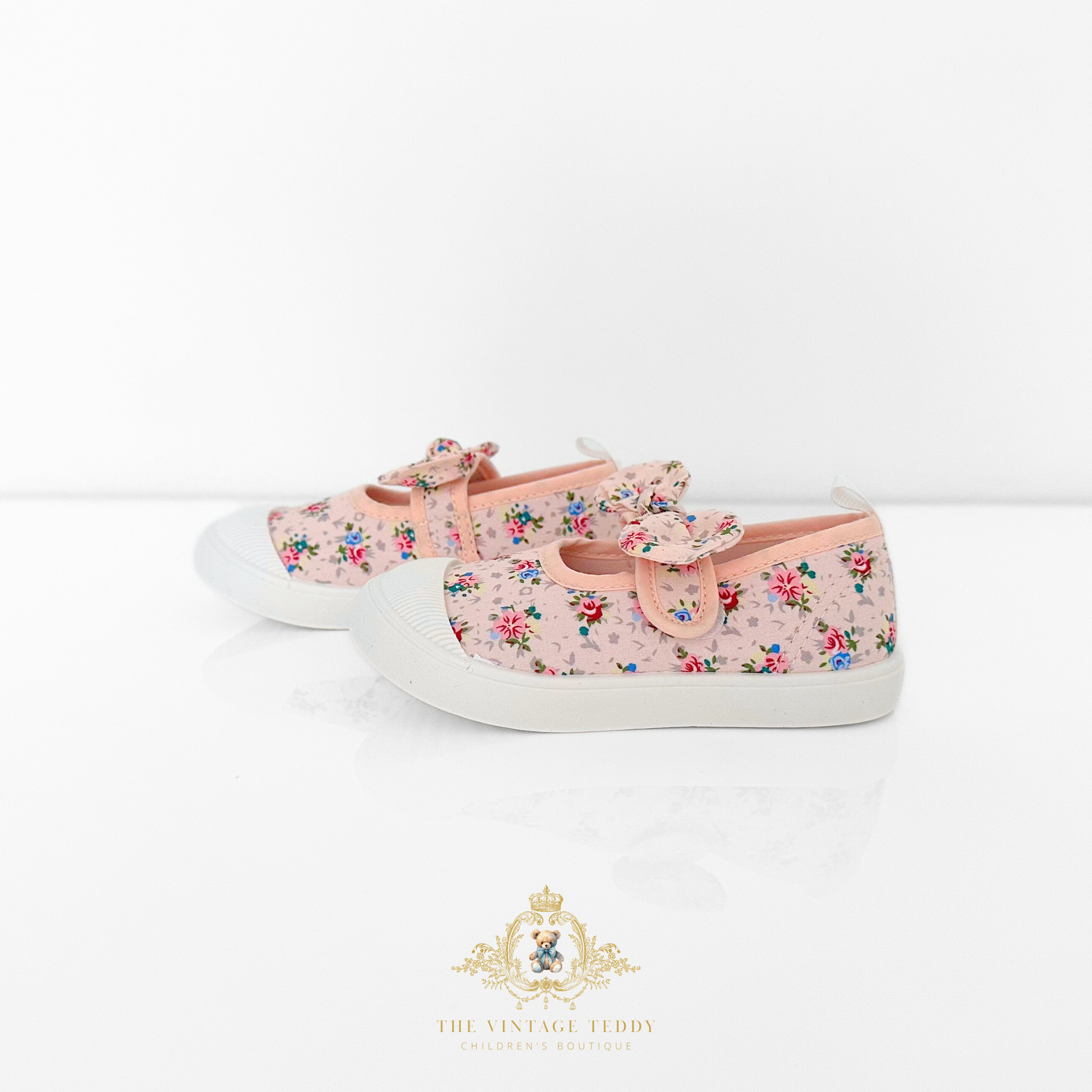 Pair of pink floral kids sneakers with white soles and pretty bow on a light background, displayed side by side.