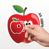 Hand holding a kids sticker with a cartoon apple design with the words an apple a day promoting healthy eating habits for kids in front of a large red apple illustration.