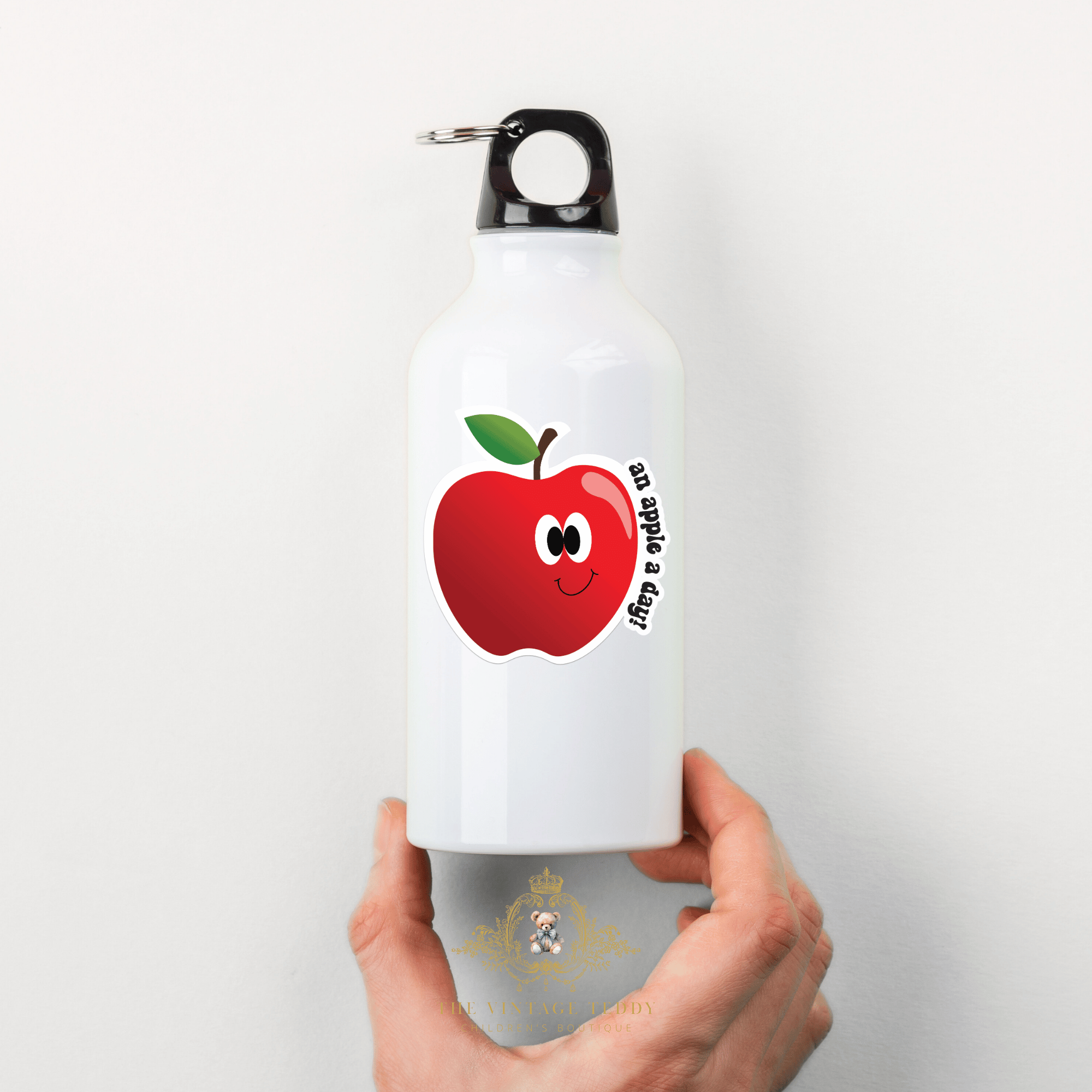 White water bottle with a red apple designed custom graphic sticker decal for kids with "an apple a day!" phrase held by a hand on a white background