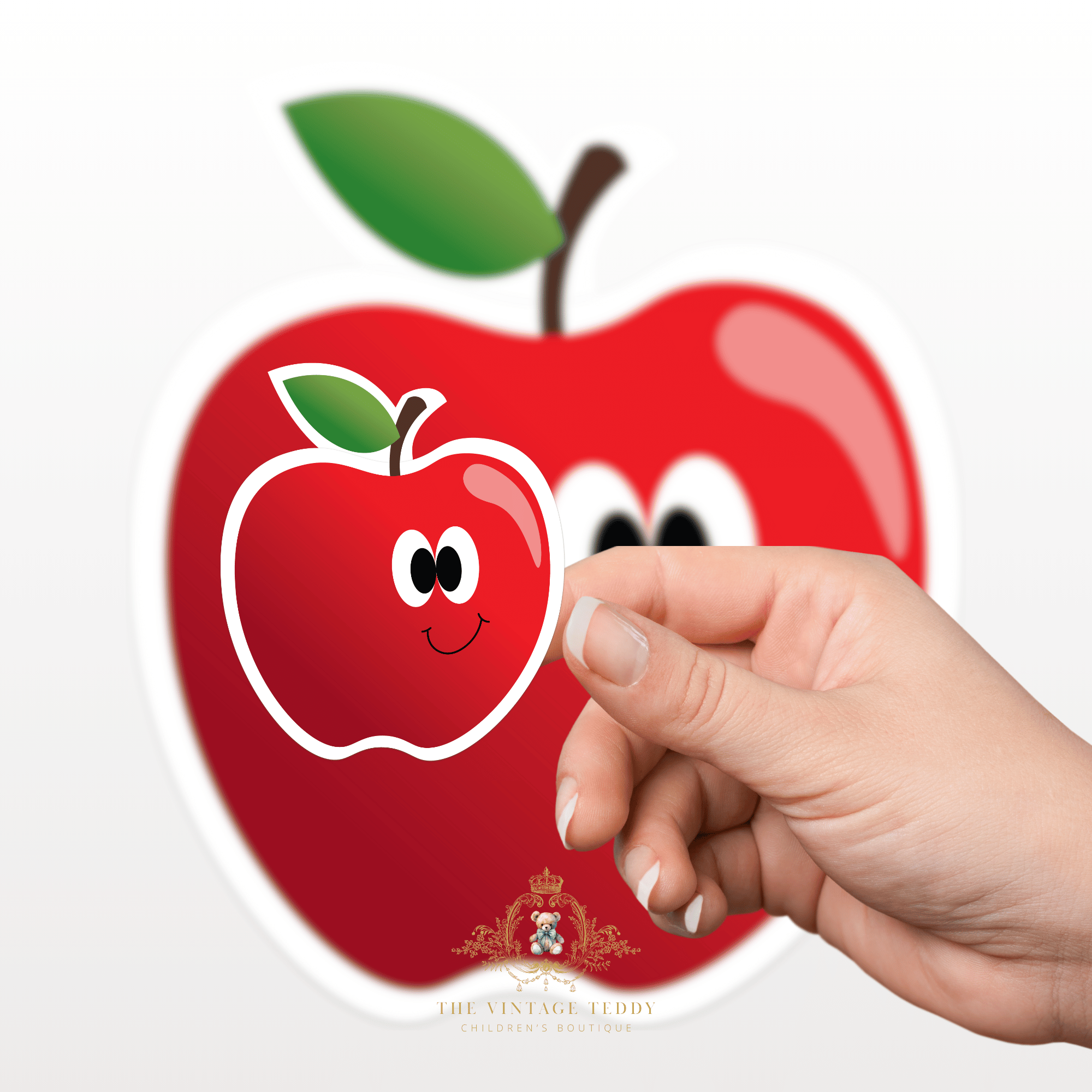 Hand holding a red apple-shaped kids sticker with cute apple character with a smiley face in front of a large red apple graphic. Custom stickers for kids