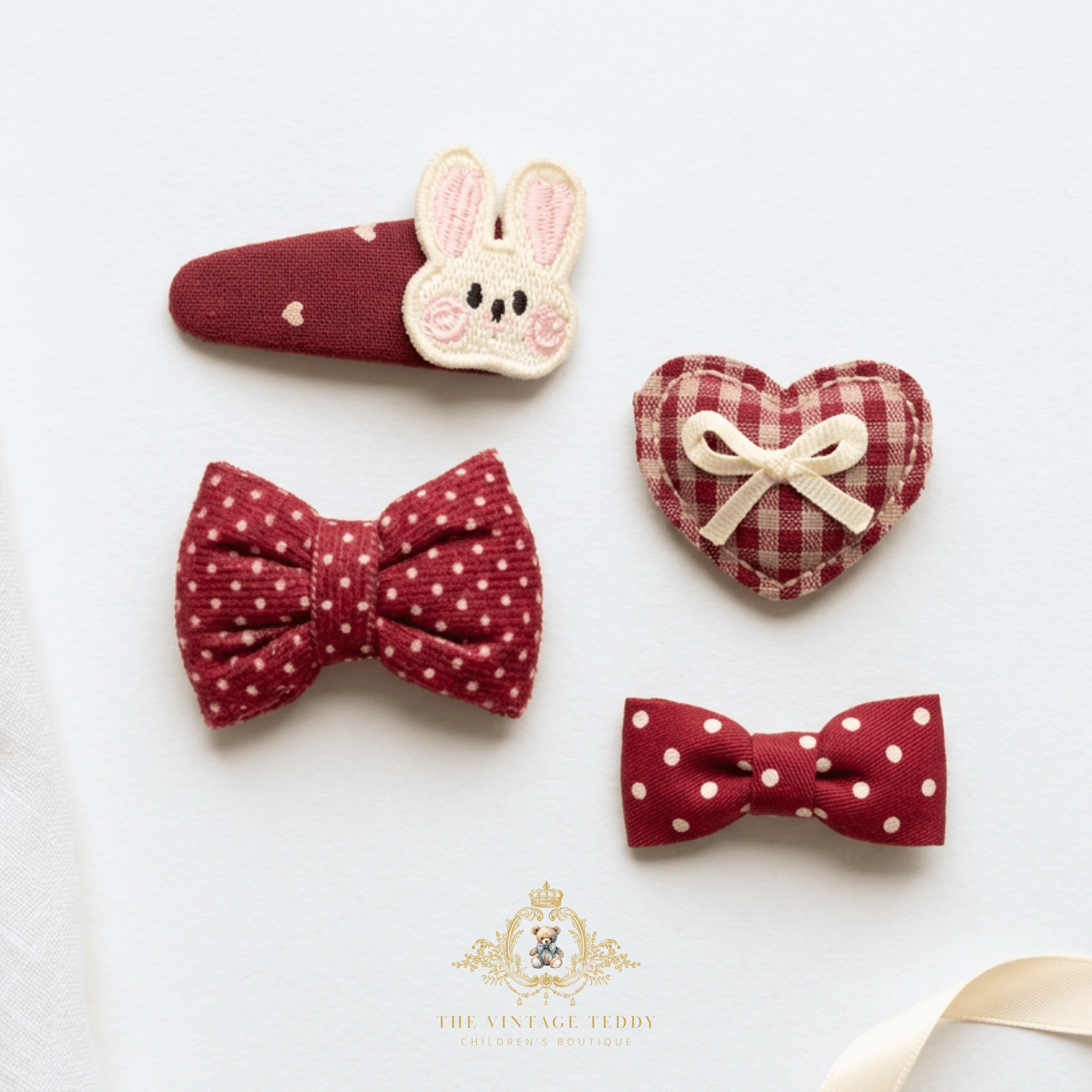 Four fabric hair accessories arranged on a white background: a red hair clip with an embroidered bunny face, a bow with white polka dots, a heart-shaped clip with a cream ribbon bow, and a bow with white polka dots. A gold watermark logo for 'The Vintage Teddy' appears at the bottom.