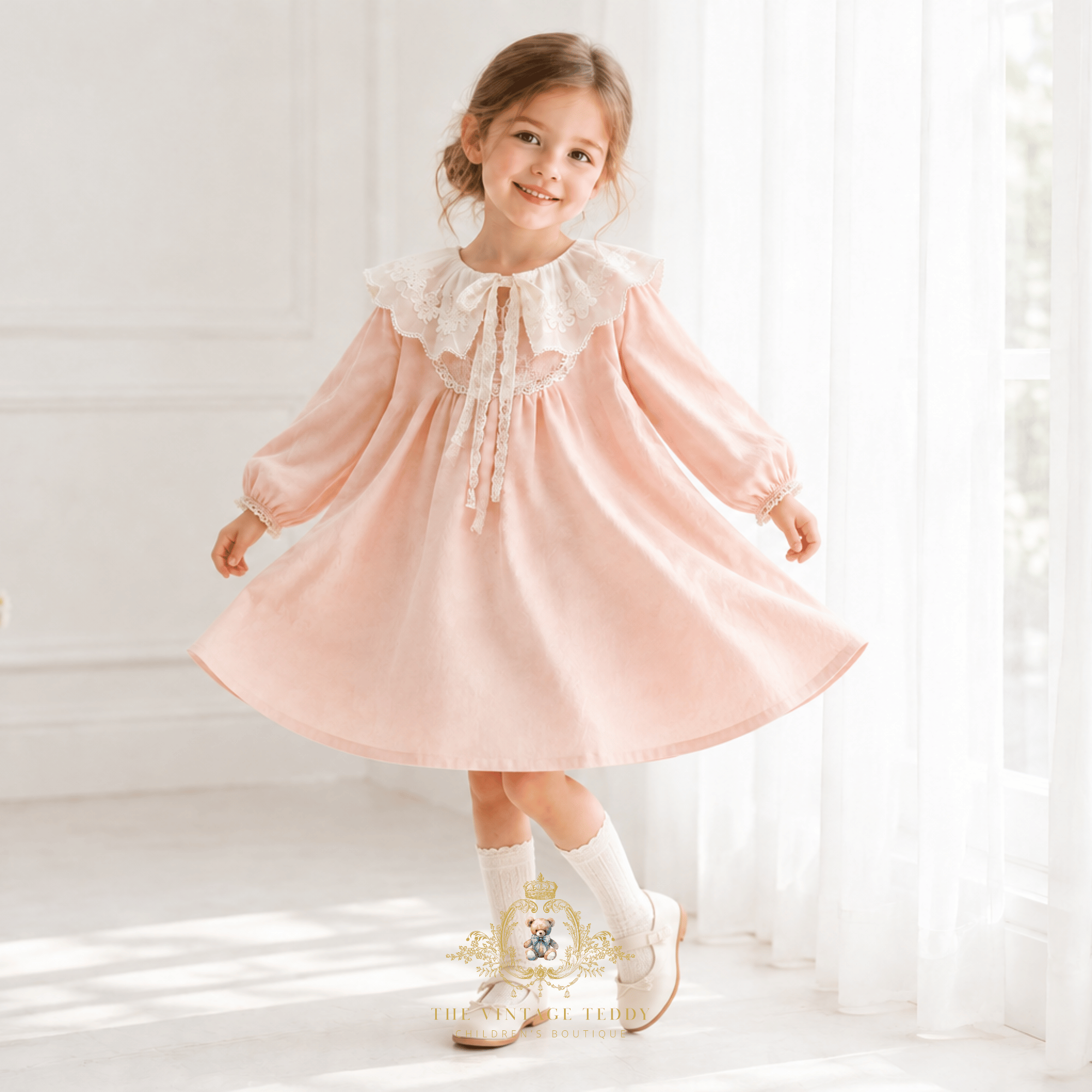 Little girl twirling and holding her dress skirt, she is smiling and wearing a blush pink children's dress with a lovely vintage-style  lace bib collar paired with white Mary Jane flats, in light an airy room by a window with sheer white curtains.