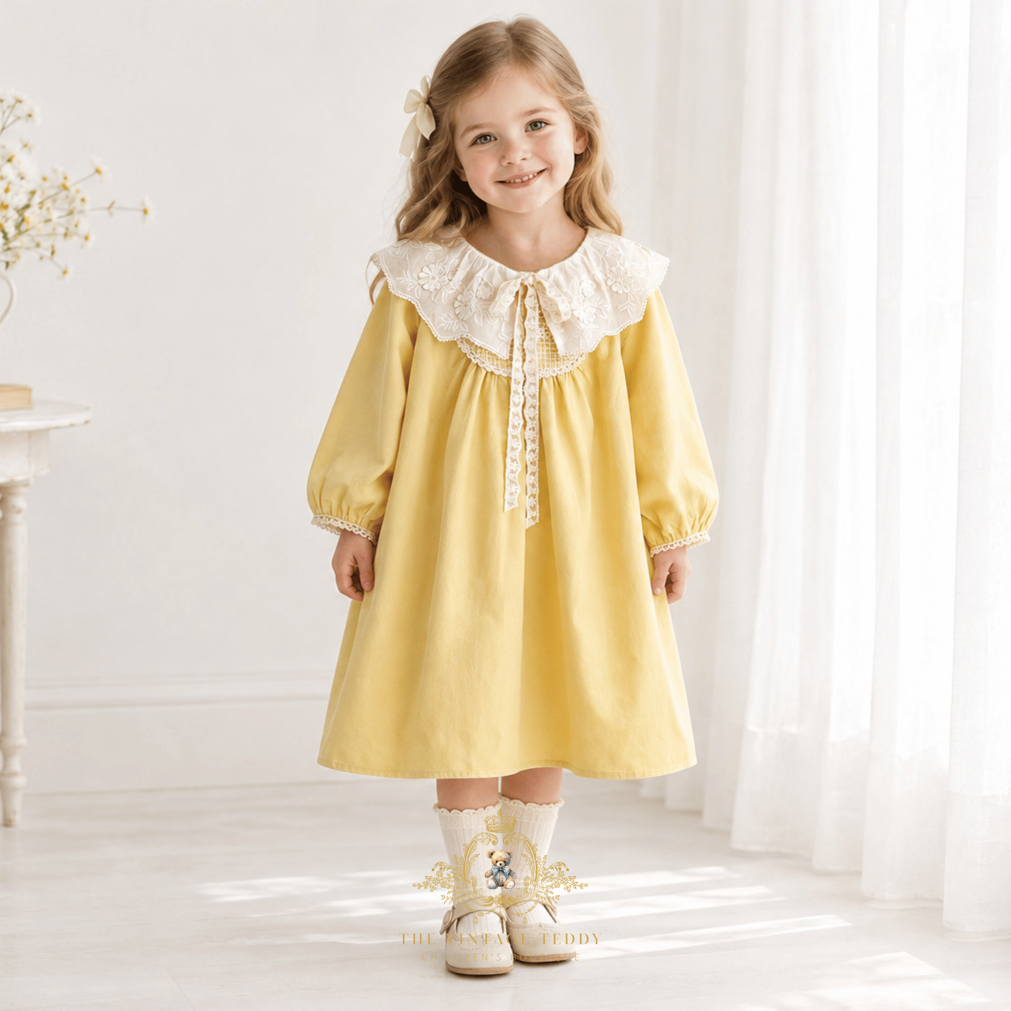 A blonde haired little girl standing in an airy light room wearing a children's dress with a  lace bib collar in a yellow fabric color with lovely lace embroidered bib collar and lace trim details and bow in cream and bishop long sleeves and Mary Jane flats in cream, she is next to a window with sheer white curtains.