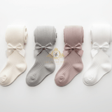 Four pairs of ribbed little girls tights with bow details, shown in cream, light gray, dusty pink, and white. A gold watermark logo for 'The Vintage Teddy' is visible in the center.
