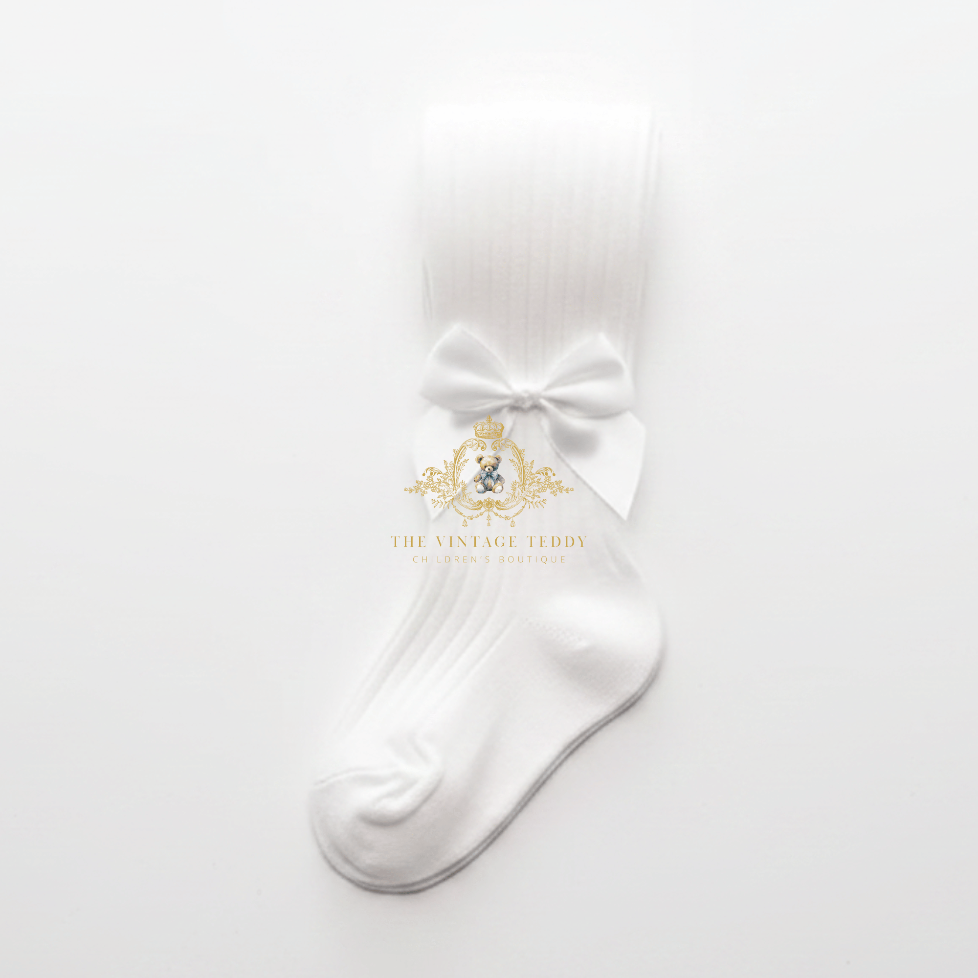 A single white ribbed children's sock with a matching white satin bow at the ankle, displayed on a clean white background with a The Vintage Teddy watermark logo in the center.