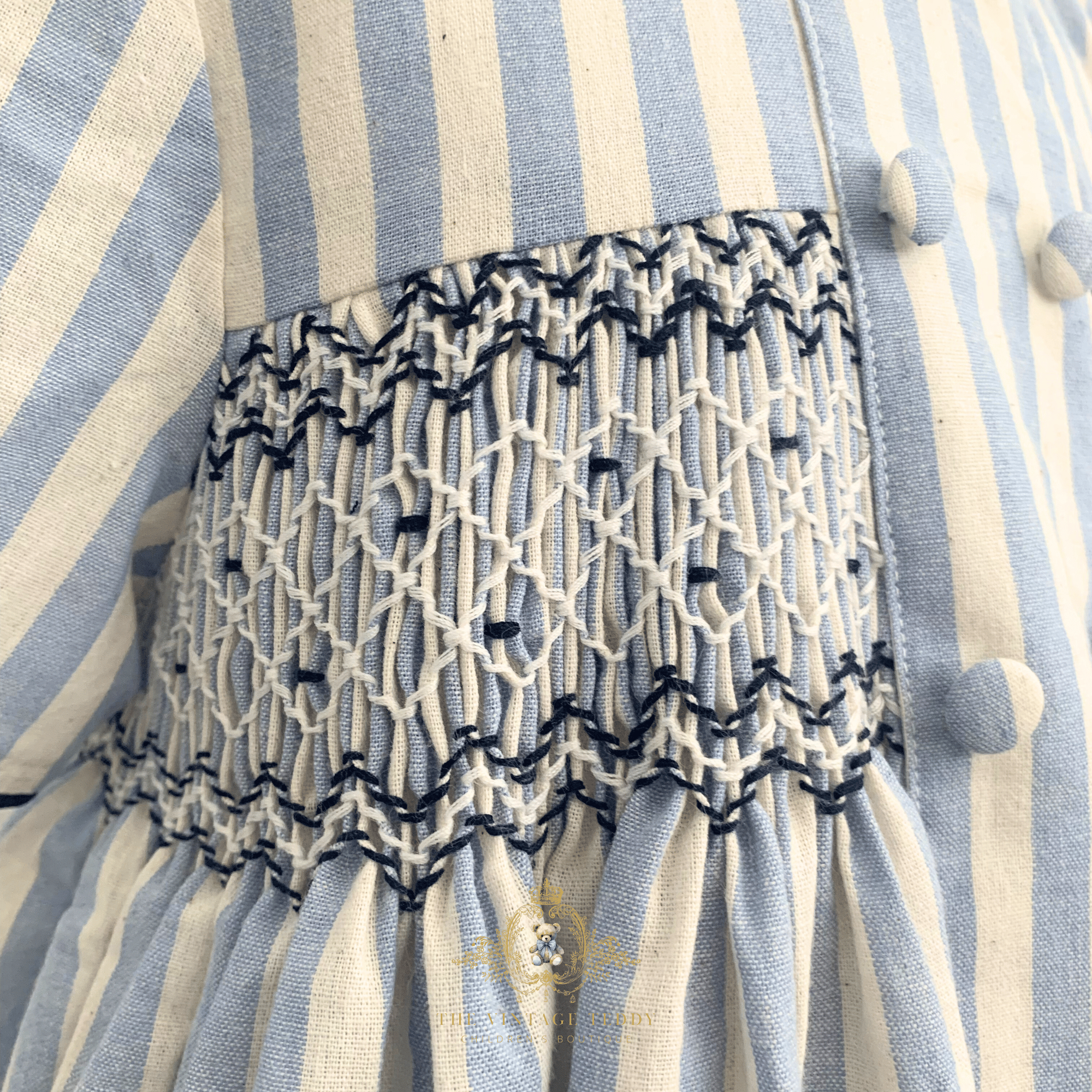 Close-up of a blue and cream striped fabric garment, kids smocked dress with a smocked waistband in white and navy blue.